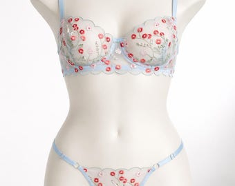 May include: Pale blue lingerie set with floral embroidery. The set comprises a scalloped-edge bra and a matching thong. The bra has adjustable straps. The floral embroidery features red and pink flowers with green leaves.
