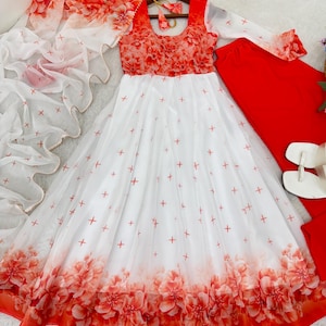 Puede incluir: Un vestido blanco y rojo con estampado floral, bufanda transparente a juego y pantalones rojos. El vestido presenta un corpiño con diseño floral y una falda adornada con cruces rojas. La bufanda transparente tiene un estampado floral.