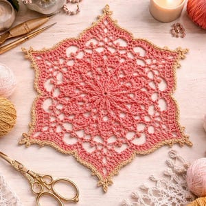 May include: A handmade, star-shaped crochet doily in shades of pink and tan. The intricate openwork design features a central circular pattern with radiating points. The doily is surrounded by a tan border. The image also includes craft supplies.