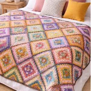 May include: A colorful, handmade crochet blanket with a patchwork design. The blanket features squares in various colors, including pink, yellow, blue, and green. The blanket is on a bed with pillows in shades of pink and yellow.