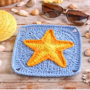 May include: A crocheted blue square with a yellow and orange starfish in the center. The image also includes a ball of yellow yarn, seashells, and sunglasses, all arranged on a wooden surface.