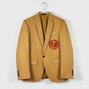 Puede incluir: Una blazer color beige con forro dorado cuelga de una percha plateada. La blazer presenta un escudo rojo y dorado en el pecho, un solo botón negro y cuatro botones en cada manga. La blazer tiene dos bolsillos delanteros.