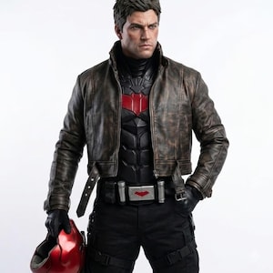 May include: A highly detailed action figure of a character with short brown hair, wearing a distressed brown leather jacket over a black tactical suit with a red chest emblem. The figure holds a glossy red helmet and wears a utility belt with a red buckle.