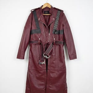May include: A long, deep burgundy coat featuring a front zipper closure, a matching waist belt with silver-toned metal buckles, black leather-like accents, shoulder epaulets, and a studded strap detail across the left chest area.