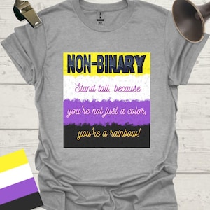 May include: A gray t-shirt with the words "NON-BINARY" in yellow and blue, and the text "Stand tall, because you're not just a color, you're a rainbow!" in white and purple. The shirt features the non-binary pride flag.