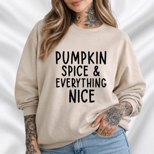 Op de afbeelding: Een beige sweatshirt met de zwarte tekst "PUMPKIN SPICE & EVERYTHING NICE". De top met lange mouwen is gemaakt van een zacht materiaal, ideaal voor de herfst.