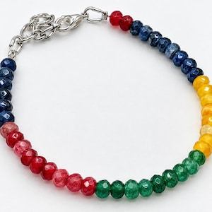 May include: A beaded bracelet featuring faceted, multi-colored stones in shades of red, blue, yellow, and green. The bracelet includes a silver-toned metal lobster claw clasp and an adjustable chain link extender for a secure fit.