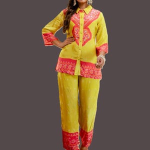 Peut inclure: Un ensemble deux pièces jaune composé d'une chemise boutonnée et d'un pantalon assorti. La chemise et le pantalon ont des bordures et des motifs rouges de style cachemire. L'ensemble est en tissu léger.