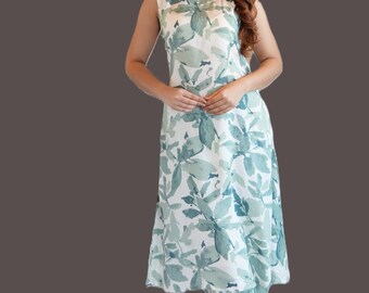 Puede incluir: Un vestido midi sin mangas con base blanca y un patrón repetitivo de hojas de estilo acuarela en verde salvia y azul cerceta. La prenda tiene un cuello redondo y una silueta recta y relajada que cae por debajo de las rodillas.