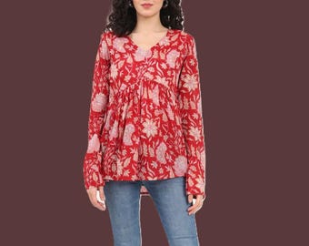 May include: A long-sleeved red blouse featuring a white floral pattern, a V-neckline, and a gathered empire waistline, paired with blue denim jeans. The blouse has a loose, flowing fit with slightly flared sleeves and a hem that falls at the hips.