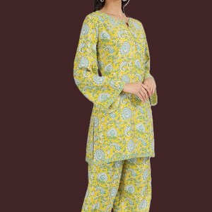 May include: A yellow two-piece pajama set with a floral design in blue and green. The top has long sleeves and a round neck, and the matching trousers complete the outfit. The fabric looks lightweight and comfortable, ideal for relaxing at home.