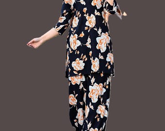 Può includere: Un completo floreale nero a due pezzi con top e pantaloni abbinati. L'ensemble è decorato con grandi motivi floreali bianchi e arancioni. Il top ha uno scollo a V e maniche a tre quarti. I pantaloni sono ampi.