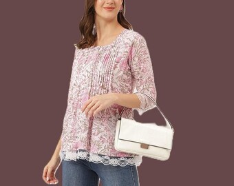 May include: A light pink and white floral print blouse with three-quarter sleeves, vertical pleats on the front, and a white lace trim at the hem. The blouse is paired with blue denim jeans and a white rectangular shoulder bag with a metallic clasp.