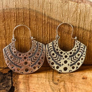 Può includere: Un paio di orecchini traforati color argento. Ogni orecchino ha una forma a semicerchio con intricati motivi geometrici, tra cui cerchi e linee. Gli orecchini hanno una chiusura a gancio.