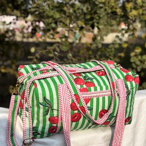 Puede incluir: Bolso de viaje rectangular a rayas verdes y blancas con estampado de cerezas. El bolso tiene una correa a rayas rojas y blancas y un peque&ntilde;o bolsillo. Dise&ntilde;ado para viajar, tiene un estilo informal.