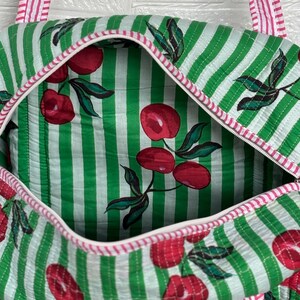 Puede incluir: Bolso tote acolchado con un estampado de rayas verdes y blancas. El bolso presenta un estampado de cerezas en el interior y el exterior. Las correas y los ribetes son de rayas rosas y blancas. El bolso tiene cierre de cremallera.