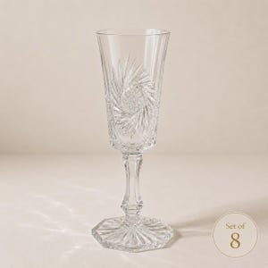 Peut inclure: Une flûte à champagne en cristal transparent ornée d'un motif taillé en étoile sur le calice, avec un pied à facettes et une base octogonale. Ce verre fait partie d'un ensemble de 8, comme l'indique l'étiquette circulaire en bas à droite.