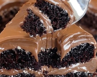 Puede incluir: Una porción de pastel de chocolate oscuro con dos capas de bizcocho húmedo y un glaseado espeso y suave de chocolate con leche. Un tenedor de metal plateado levanta un trozo, mostrando la textura densa y el glaseado cremoso y brillante.