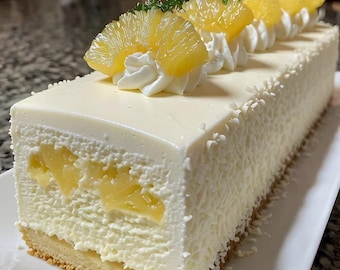 Puede incluir: Un postre rectangular con glaseado blanco, decorado con crema batida y rodajas de piña. El pastel tiene una capa visible de relleno de piña y se asienta sobre una base de galleta. Los lados están cubiertos con copos blancos.