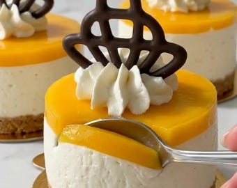 Puede incluir: Tres tartas de queso individuales redondas con una cobertura de fruta amarillo dorado, un centro cremoso blanco y una base de migas marrón claro. Cada tarta tiene un copete de nata montada blanca y una pieza decorativa de chocolate oscuro.