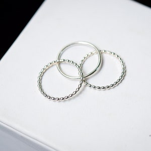 May include: Three silver beaded rings stacked on a white surface.