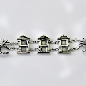 May include: Silver bracelet with three house charms and two tree charms. The house charms have a detailed design with windows and brickwork. The tree charms are stylized and have a rustic look.