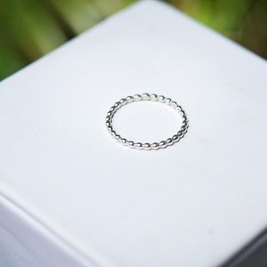 May include: A silver beaded ring on a white background.