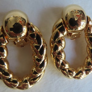 May include: A pair of gold-tone clip-on earrings with a twisted rope design. The earrings are oval shaped and have a smooth, polished finish.