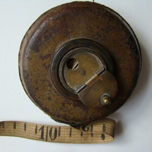 May include: A vintage brass measuring tape with a leather case. The tape is extended and shows the number "110" in black.