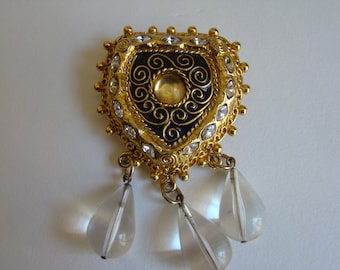 May include: A gold-tone heart-shaped brooch with clear rhinestones and a black enamel center with gold filigree. Three clear teardrop-shaped pendants hang from the bottom.