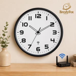 May include: A round wall clock with a black frame and a white face featuring bold black Arabic numerals. The clock has black hour, minute, and second hands, and a small Wi-Fi signal icon printed above the number six on the dial.