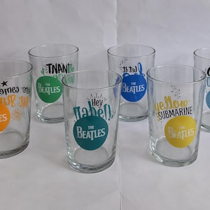 Peut inclure: Un ensemble de six verres transparents, chacun orné d'un titre de chanson des Beatles et d'un motif circulaire coloré. Les designs incluent Here Comes The Sun en orange, In My Life en vert, Hey Jude en sarcelle, Let It Be en bleu, Yellow Submarine en jaune et Come Together en bleu clair.