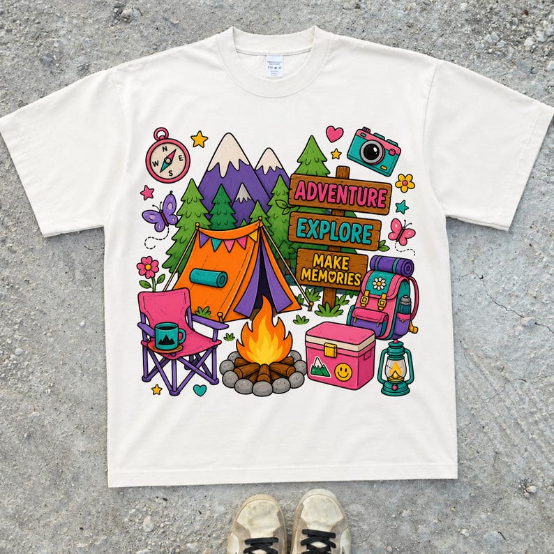 May include: White t-shirt featuring a camping-themed illustration. The design includes a tent, mountains, a compass, a camera, and the words "Adventure, Explore, Make Memories." Other elements include a campfire, backpack, and a lantern.