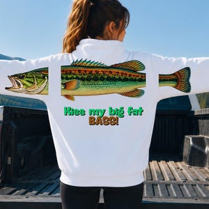 May include: A white long-sleeve hooded sweatshirt featuring a graphic of a green and yellow largemouth bass fish split into three segments across the back. Below the fish, the text reads "Kiss my big fat BASS!" in green and brown lettering.