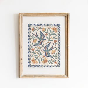 May include: A framed mosaic-style print featuring two blue and orange birds flying among stylized floral vines. The artwork is enclosed by a decorative border of blue and white waves, all set within a light-toned wooden frame with a white mat.