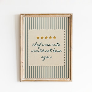 May include: A framed wall art print featuring a beige background with vertical dark gray stripes. Centered is a scalloped-edge cream square with five gold stars and the dark green text: chef was cute would eat here again.