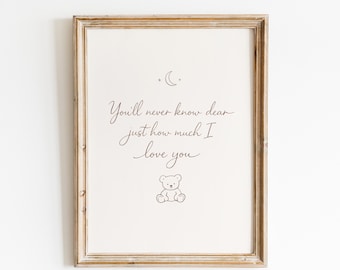 Op de afbeelding: Een ingelijste wandprint met een lichte achtergrond, een donkerbruin maansikkel-icoon bovenaan, de tekst "You'll never know dear just how much I love you" in cursief schrift en een kleine lijntekening van een teddybeer eronder.