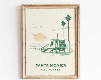 May include: Framed print featuring a green and beige illustration of a lifeguard station on a beach at sunset. The words "Santa Monica California" are printed below the image. Palm trees and a surfboard are also visible.
