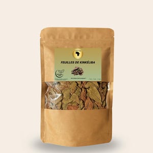 May include: A brown paper bag with a clear window displaying dried green and brown leaves. The bag has a label with the text "FEUILLES DE KINKÉLIBA" and a logo. The bag is sealed and sits against a light background.