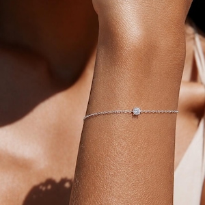 Peut inclure: Un bracelet à chaîne délicat de couleur argentée doté d'une petite pierre ronde transparente à facettes sertie au centre. Le bracelet se compose de fins maillons métalliques entrelacés qui entourent le poignet, créant une apparence raffinée.