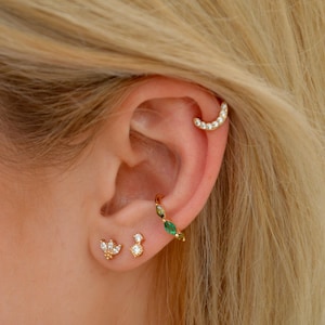 Peut inclure: Un anneau de cartilage doré orné d'une rangée de pierres claires, une boucle d'oreille dorée avec des pierres taille marquise vertes et claires alternées, et deux petites boucles d'oreilles dorées, l'une avec un groupe de pierres et l'autre avec une pierre.