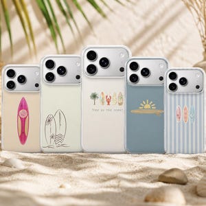 Könnte beinhalten: Fünf transparente Smartphone-Hüllen mit verschiedenen Surf-Motiven. Die Designs umfassen ein pinkes Surfbrett, Surfbretter als Strichzeichnung mit Blumen, eine Reihe von Surfbrettern mit einem Hummer und dem Text 'free as the ocean', eine Sonne über einem Surfbrett.