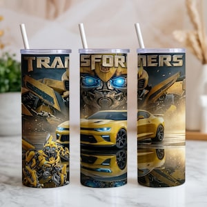 May include: Three cylindrical tumblers with white straws, each featuring a Transformers graphic. The design displays a yellow sports car, a robotic character, and the word Transformers in metallic lettering against a dark, smoky background.