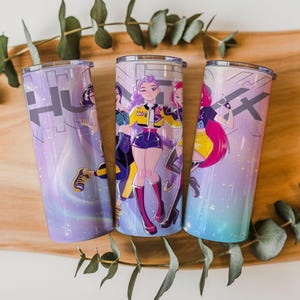 Puede incluir: Tres vasos de acero inoxidable con un diseño de estilo anime colorido. Cada vaso presenta un personaje diferente en colores vibrantes, sobre un fondo degradado de morado, azul y rosa. Los vasos miden aproximadamente 20 cm de alto.