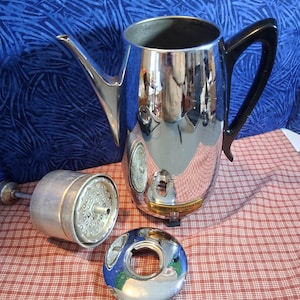 May include: A vintage chrome Universal Coffeematic coffee pot with a black handle, a spout, and a detachable filter basket. The pot is highly reflective, with a lid and a separate ring. The items are on a red and white checkered surface.