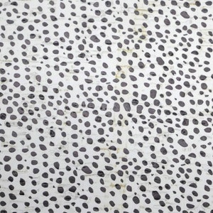 May include: White fabric with a black polka dot pattern. The fabric has a slightly textured surface. A ruler is visible at the bottom of the image.