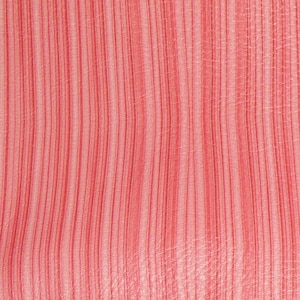 May include: Close-up of a textured, coral-colored fabric with vertical, thin, darker red stripes. The fabric has a subtle sheen and a slightly irregular pattern. A metal ruler is at the bottom of the image.