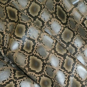 May include: Close-up of a fabric with a snakeskin pattern. The material features a repeating diamond pattern in shades of grey, brown, and tan. The fabric has a slight sheen, and the pattern is detailed and textured.