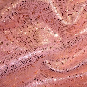 May include: Pink fabric with a gold snakeskin pattern. The fabric is shiny and has a glittery texture.