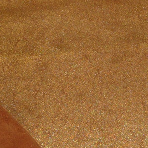 Könnte beinhalten: Nahaufnahme eines braunen Wildleders mit einem goldenen Glitzerstoff darunter. Der Glitzerstoff hat einen dezenten irisierenden Schimmer.